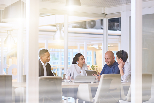 Four corporate board members at a table discussing directors and officers insurance, sunlight reflecting on glass walls.